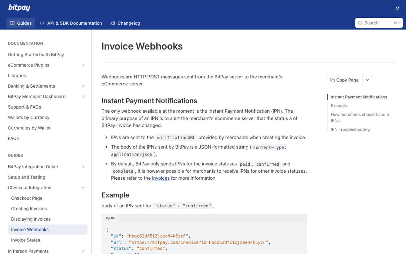 Screenshot of BitPay's developer documentation page Invoice Webhooks, captured 27 September 2026, stating that the only webhook available is the Instant Payment Notification, that IPNs are sent to the notificationURL provided when creating the invoice, that the body is a JSON-formatted string, and that BitPay sends IPNs for the paid, confirmed and complete invoice statuses by default